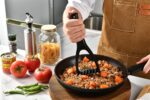 Black nylon potato masher with an ergonomic handle, resting on a white background, showcasing its non-scratch design.