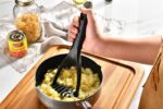 Black nylon potato masher with an ergonomic handle, resting on a white background, showcasing its non-scratch design.