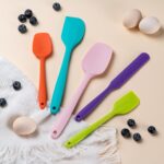 A set of five multicolor silicone spatulas with stainless steel cores, arranged for a kitchen product display.